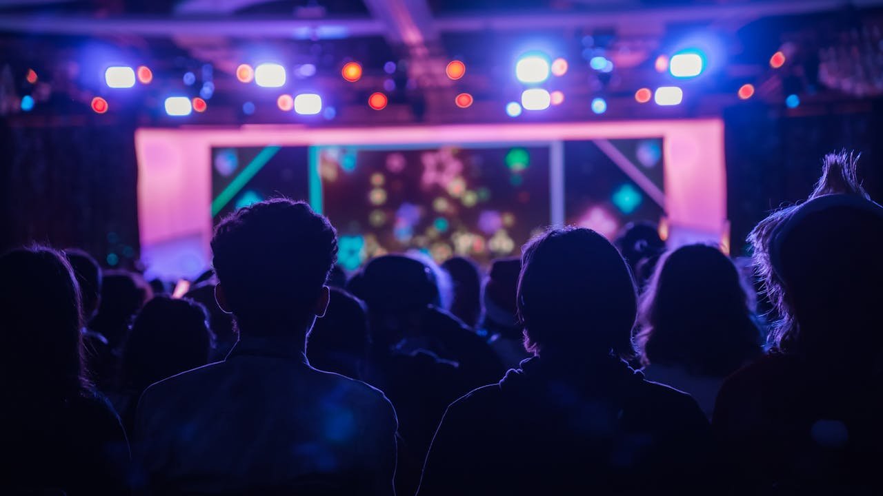 Back view of people at a concert with colorful stage lights creating a vibrant atmosphere.