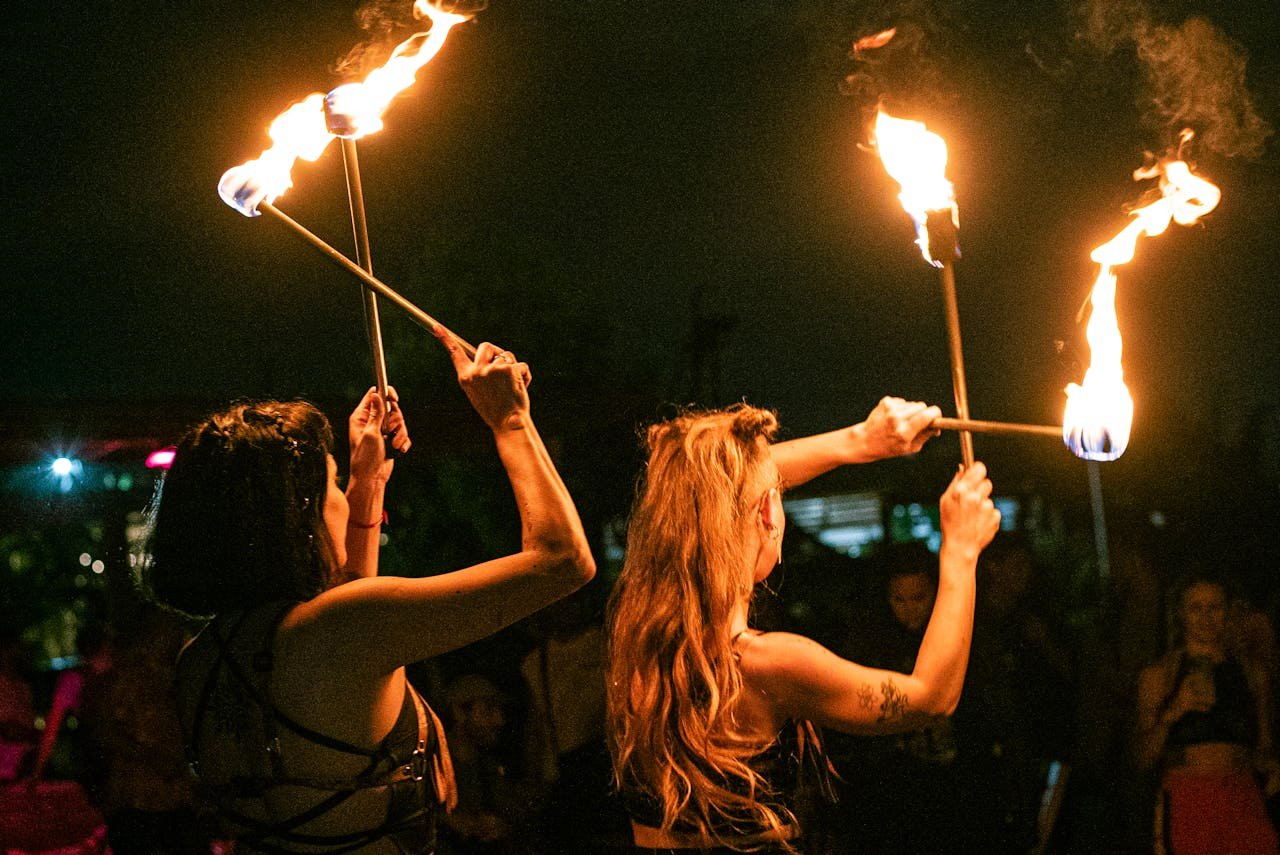 Two women perform an exhilarating fire dance with flaming sticks at a nighttime festival.