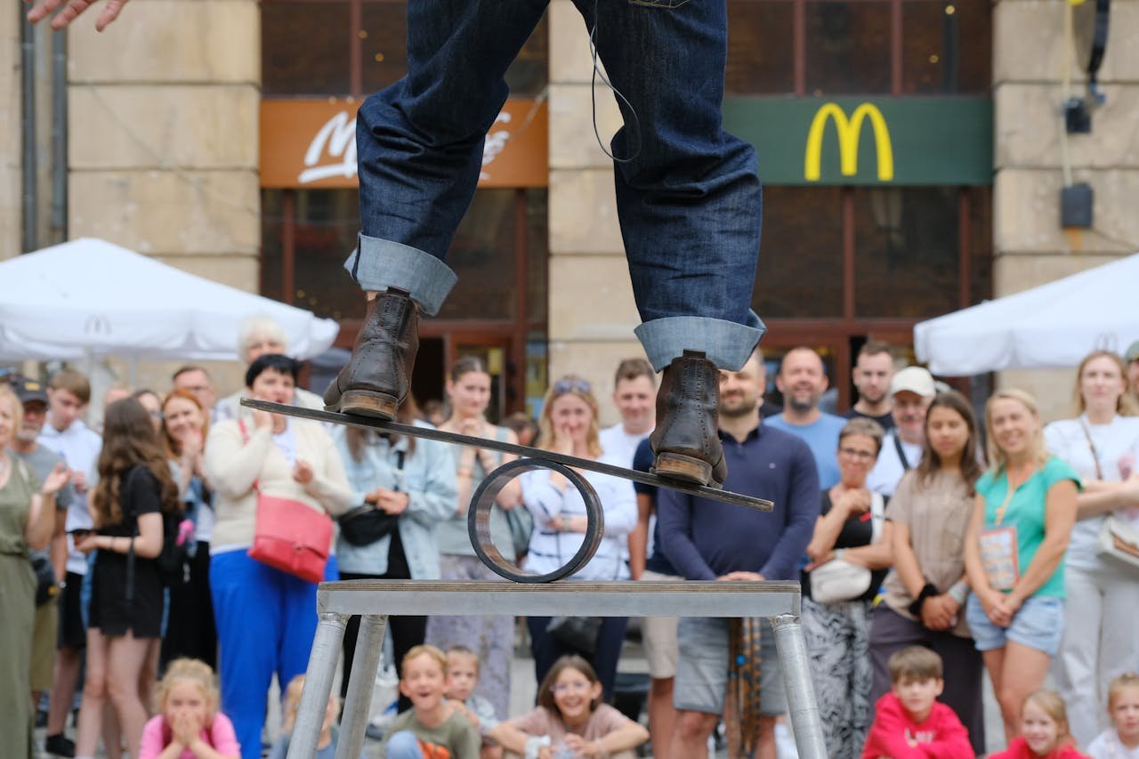 A street performer skillfully balances on a metal structure, captivating a crowd in an urban setting.